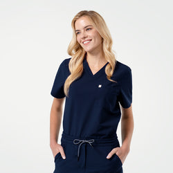 Image of Smiling model wearing an Eco Navy scrub top with a single pocket, posing with hands in pockets.