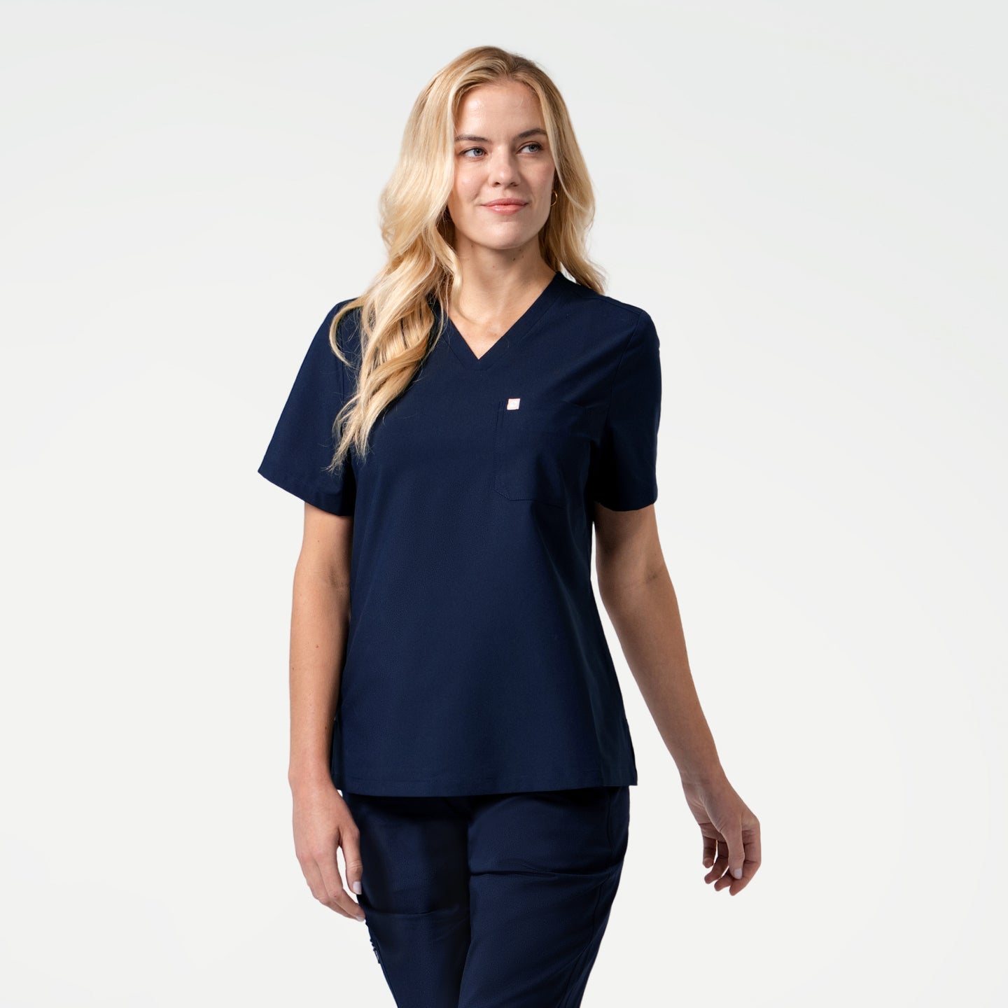 Image of Model dressed in the Women's Eco Navy Single Pocket Scrub Top, looking away with a relaxed expression, full body shot