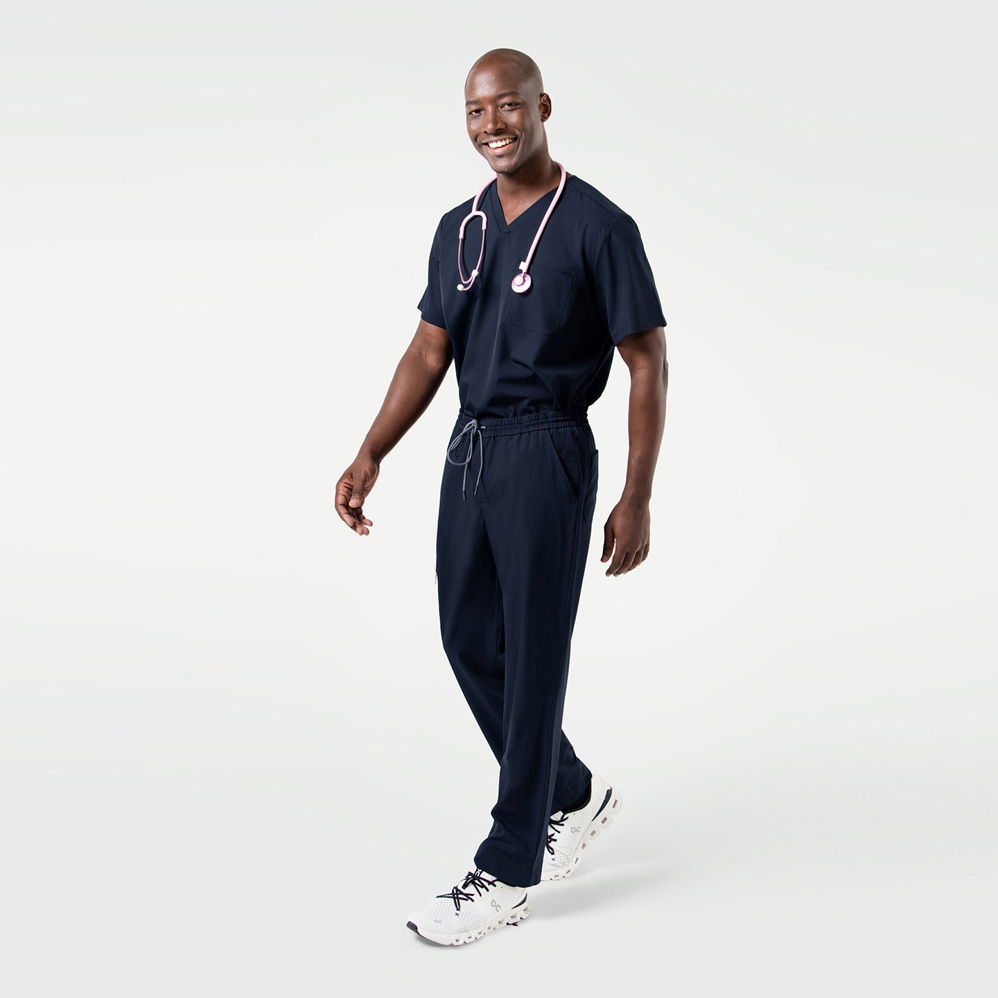 Image of Wearing the Eco Navy Single Pocket Scrub Top, the model takes a step with a relaxed, smiling expression.