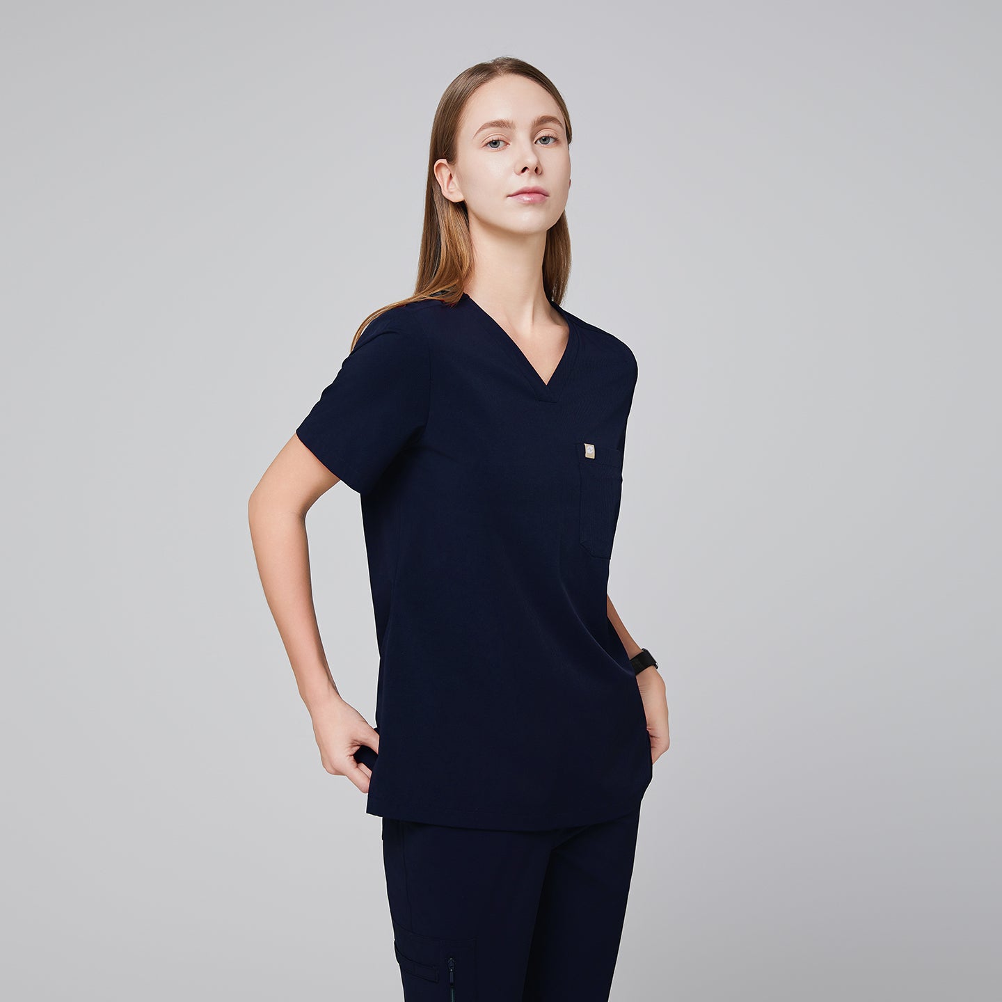 Navy scrub top with single pocket paired with matching scrub pants, with hands by the side of their waist,Eco navy