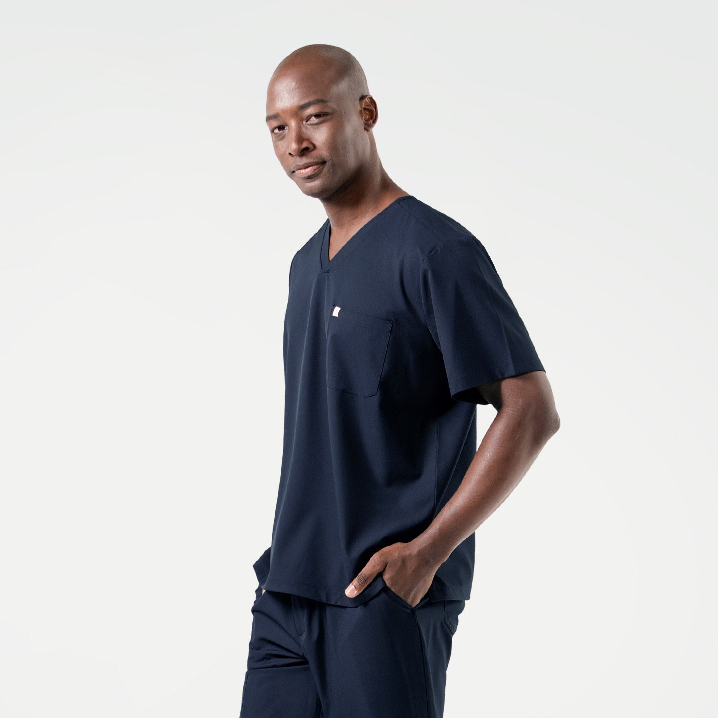 With one hand in his pocket, the male model wears an Eco Navy scrub set and looks slightly to the side with a composed expression.