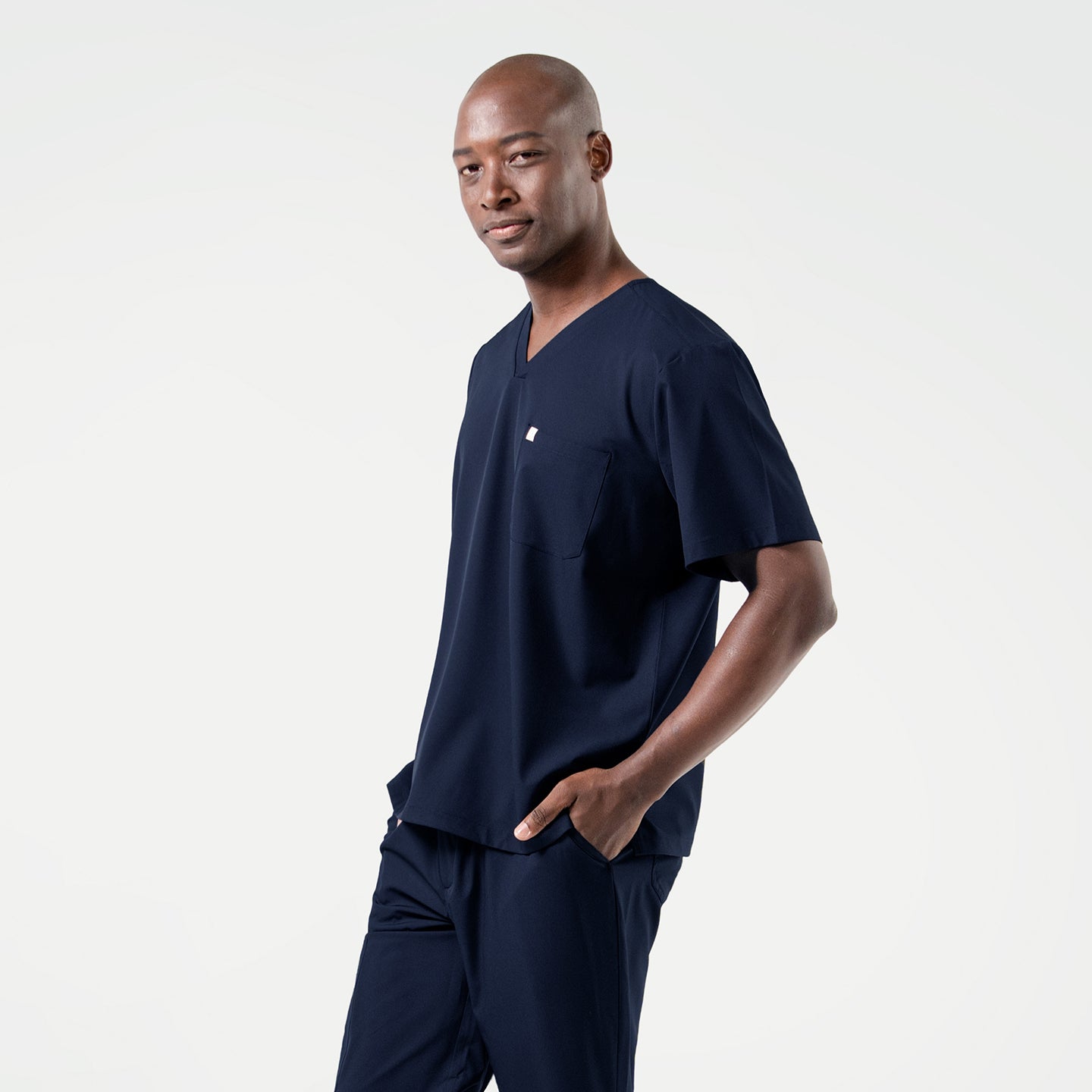 Image of With one hand in his pocket, the male model wears an Eco Navy scrub set and looks slightly to the side with a composed expression.