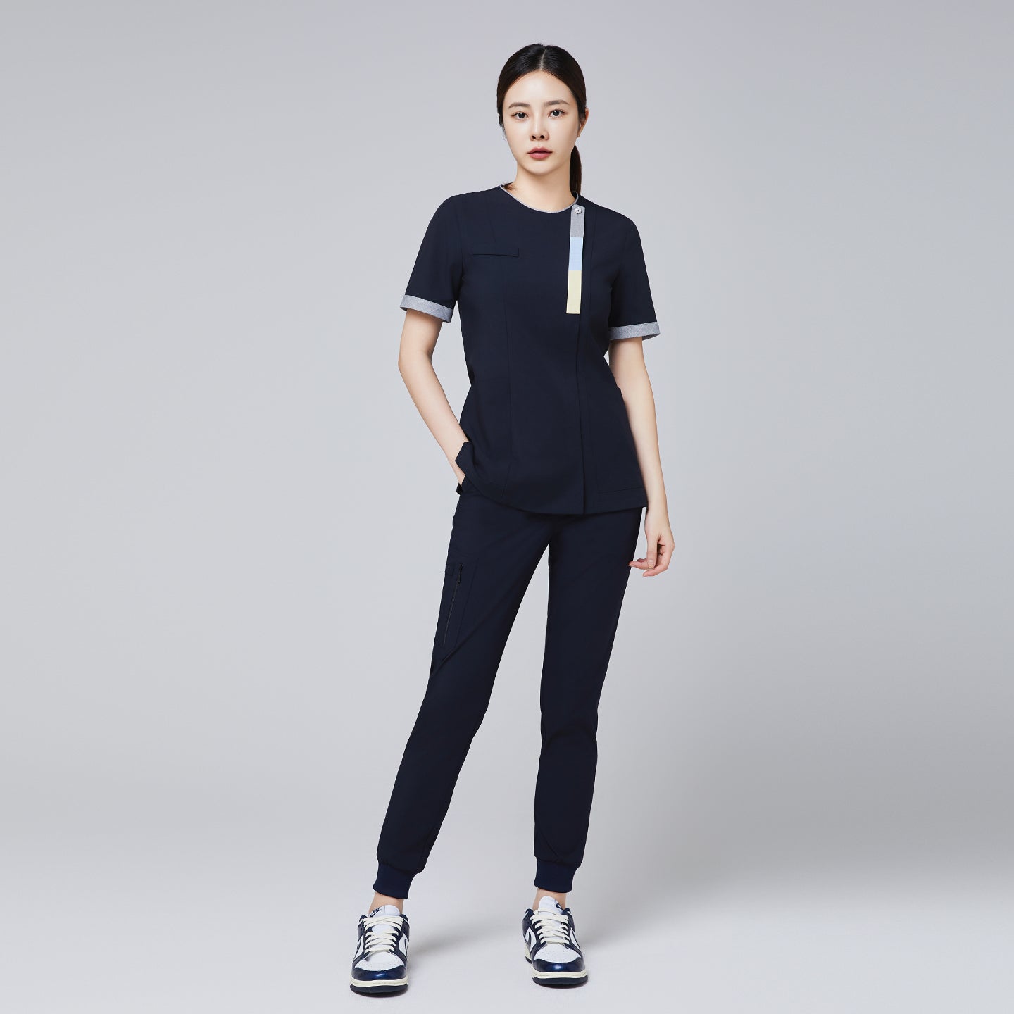 Image of Full-body view of a woman wearing a navy scrub set with triple-tone accents, paired with sneakers, ideal for medical professionals,Eco Navy