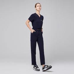 Image of Full-length shot of a female model wearing Zenir Women's Zipper Pocket Split Hem Scrub Pants in Eco Navy, featuring a comfortable elastic waistband, secure zipper pockets, and a stylish split hem detail in a clinical setting.