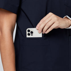 Image of Hand placing a phone into the pocket of an eco navy scrub top, showcasing convenient pocket design,Eco Navy