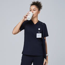 Image of Model in navy V-neck scrub top with shoulder buttons, drinking from a cup and wearing a Zenir badge,Eco Navy