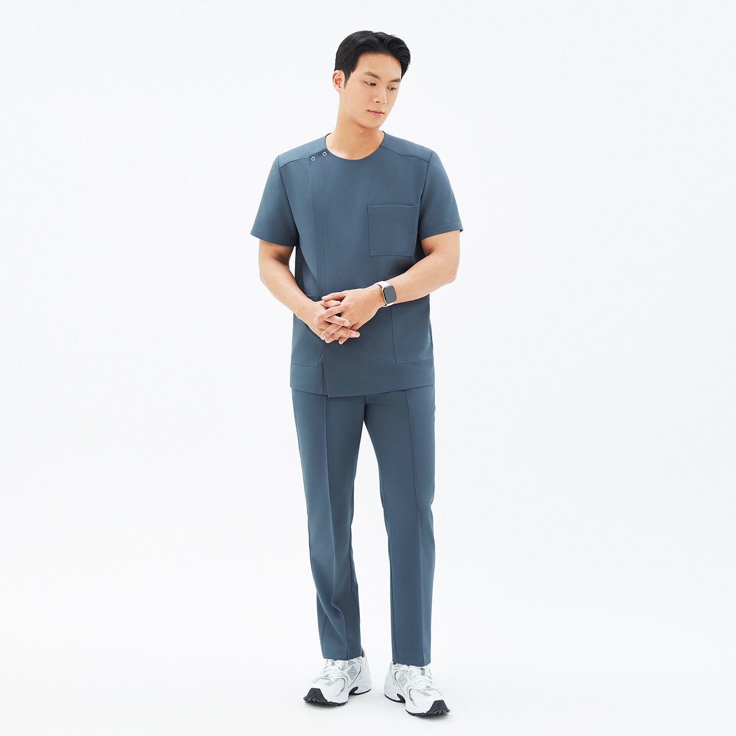 Full-body shot of a male model wearing TUL Men's Premium Banding Pants in Haze Gray, hands clasped, paired with a matching scrub top.
