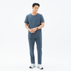 Image of Full-body shot of a male model wearing TUL Men's Premium Banding Pants in Haze Gray, hands clasped, paired with a matching scrub top.