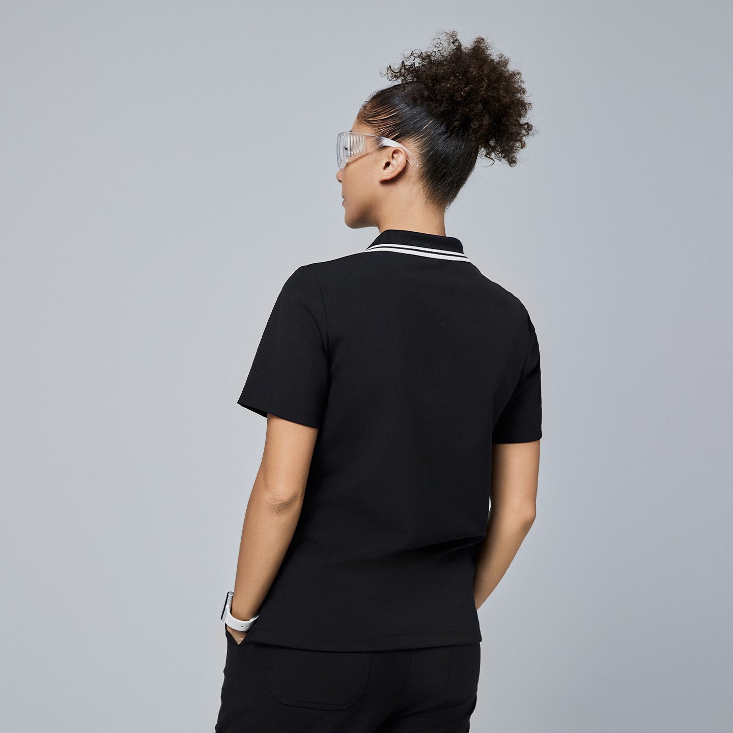 Image of Back view of a woman wearing a black polo scrub top with a white striped collar, paired with black pants,Jet Black
