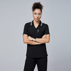 Image of Female model wearing a jet black essential polo scrub top with a striped collar, arms crossed, accessorized with safety glasses and a smartwatch,Jet Black