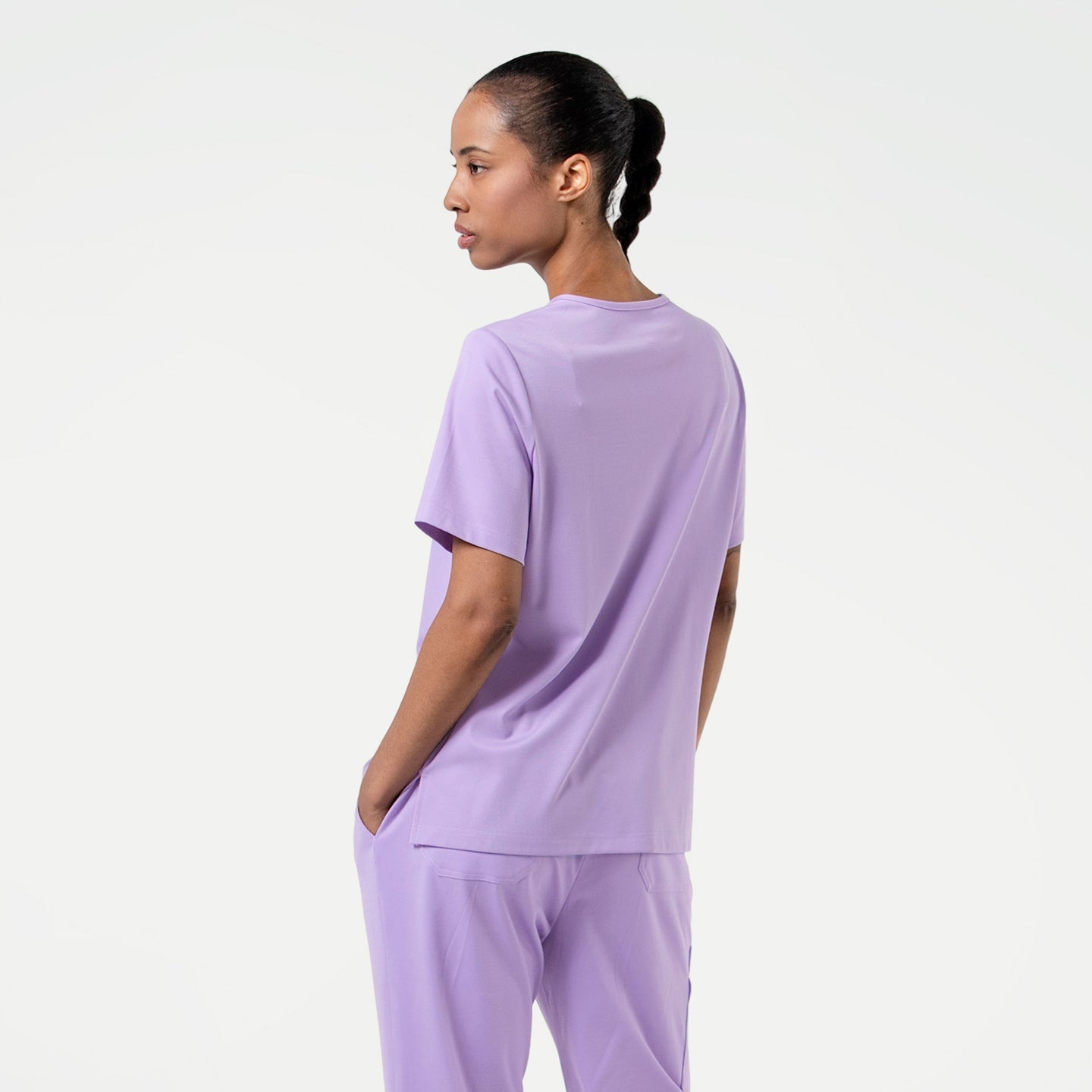 Image of Back view of a model wearing a Lavender scrub top against a light background.
