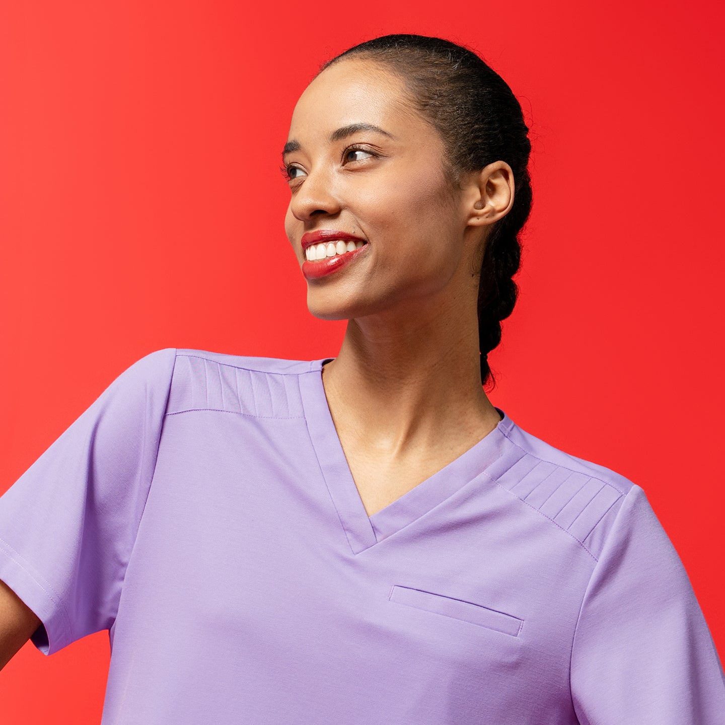 Image of Close-up of the Women's Lavender Pleated Shoulder Scrub Top with pleated shoulder detail, red backdrop, upper body view