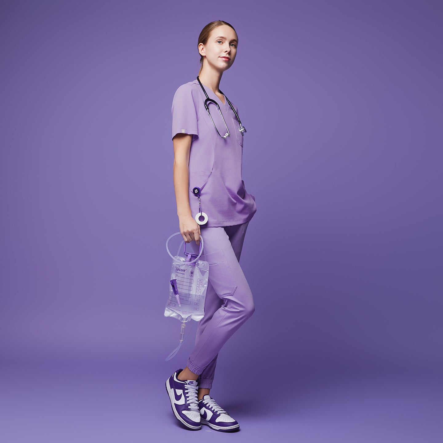Woman dressed in a lavender scrub set, holding a medical fluid bag, standing confidently against a matching lavender backdrop,Lavender