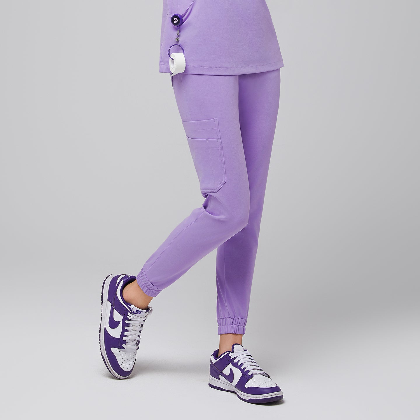 Image of Female wearing lavender jogger scrub pants with side pockets, paired with purple and white sneakers,Lavender