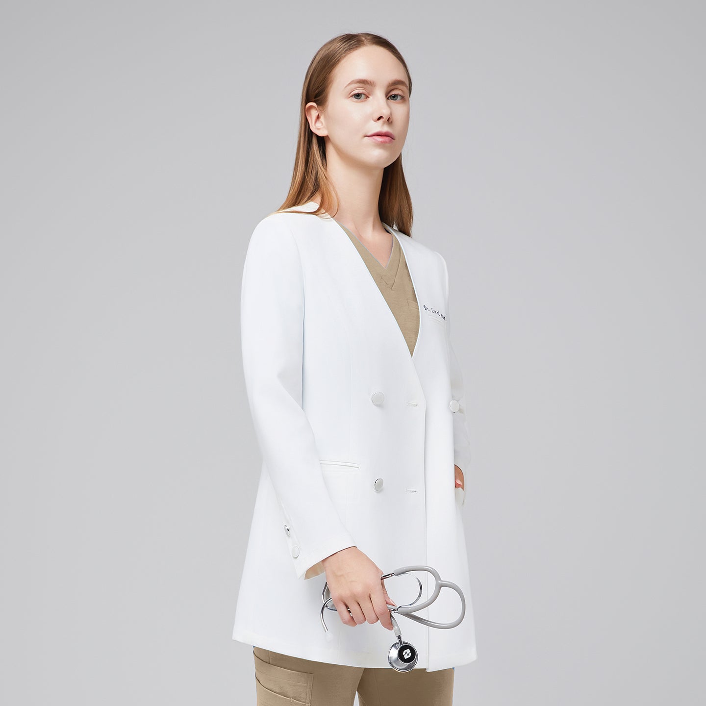 Image of A woman wearing a white long lab coat (LCW-09) over a Sand Beige Pleated Shoulder Scrub Top and Sand Beige Straight Split Hem Scrub Pants, holding a stethoscope in her hand,White