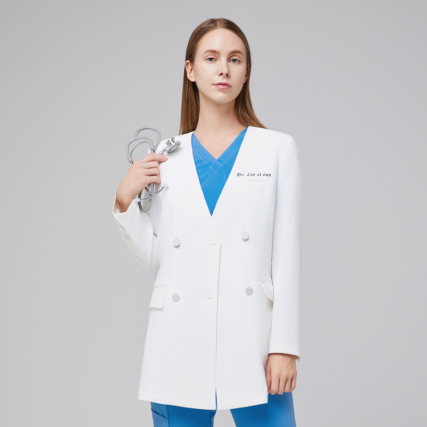 A woman wearing a white long lab coat (LCW-09) over an Aqua Blue Pleated Shoulder Scrub Top and Aqua Blue Straight Split Hem Scrub Pants, holding a stethoscope,White