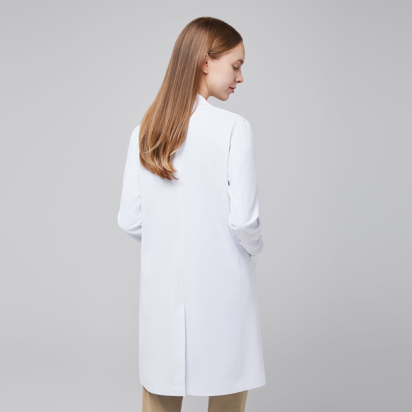 Image of Back view of a woman wearing Zenir’s Women’s White Long Lab Coat LCW-10 over Sand Beige scrubs, highlighting the coat’s length and back design,White