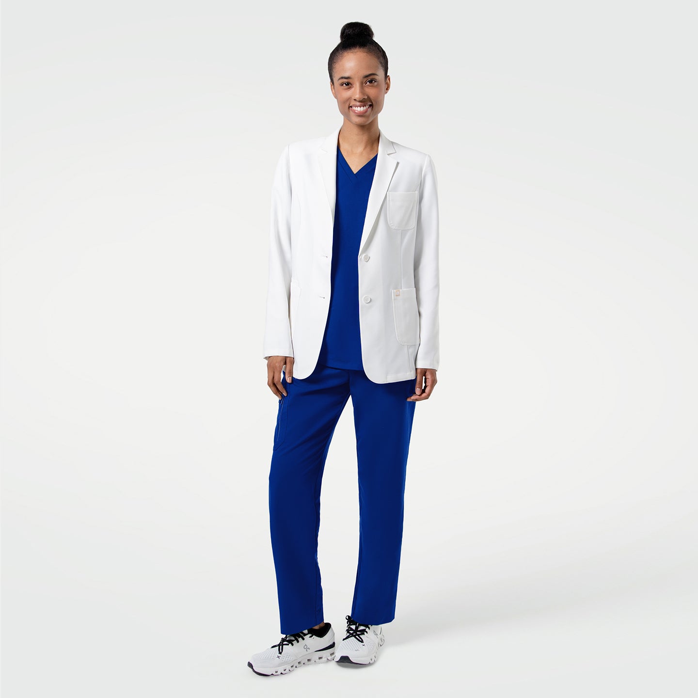 Image of Standing confidently with a relaxed smile, the model showcases the LCW-201 lab coat layered over vibrant royal-blue scrubs, emphasizing the coat’s clean structure, modern tailoring, and smooth upgraded fabric that creates a crisp, professional silhouette.