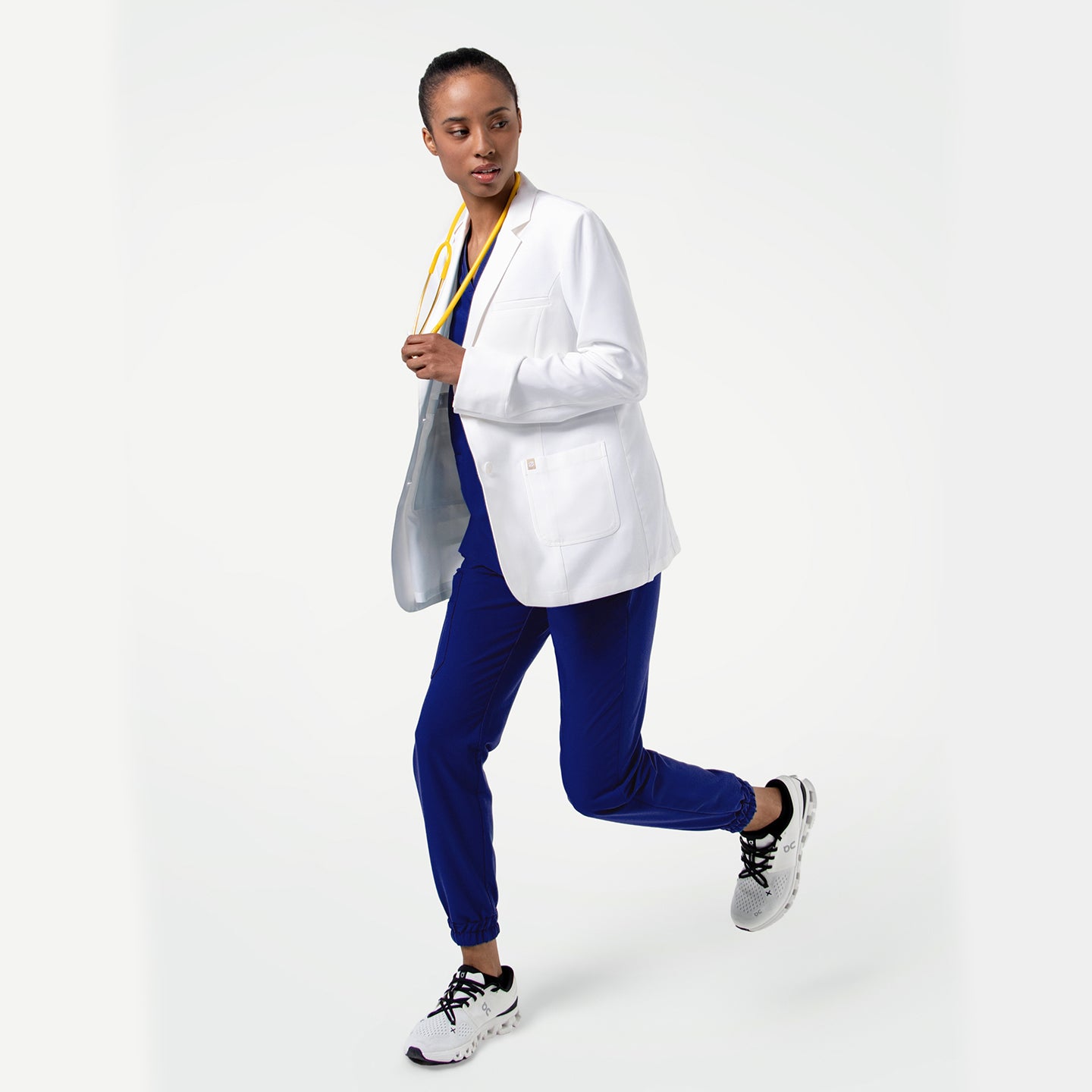 Image of Captured in mid-stride, the model showcases the LCW-202 lab coat’s dynamic, modern fit, highlighting how the coat maintains a clean, structured silhouette even during movement, with its smooth white fabric and front patch pockets creating a polished professional look.