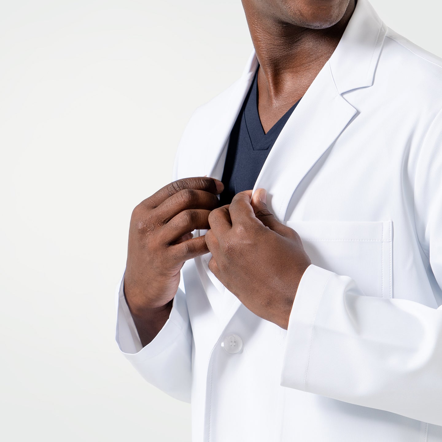 Image of Close-up view of a male model adjusting the LCM-02 White Lab Coat, revealing Eco Navy scrubs underneath.