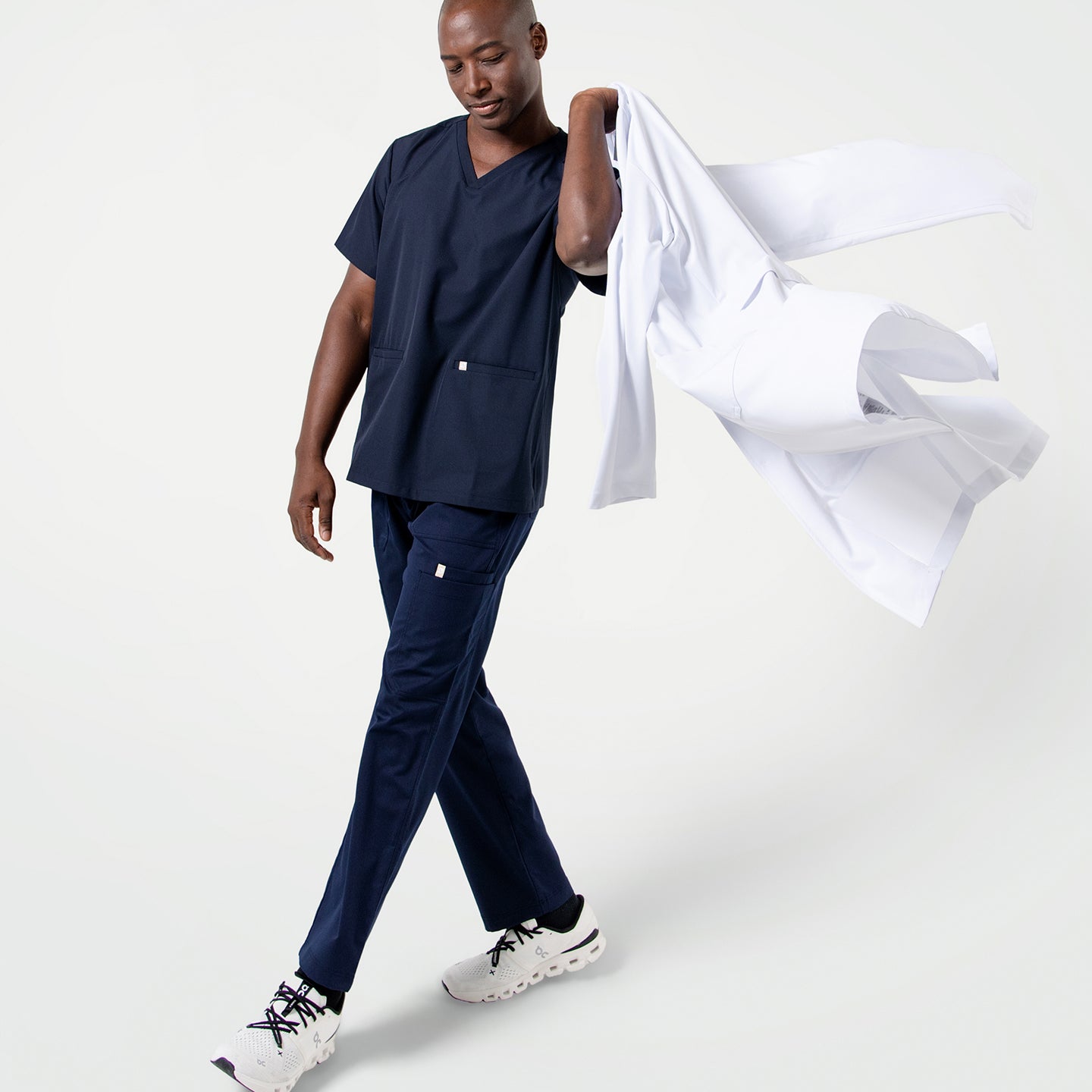 Image of Male model in Eco Navy scrubs walking with a relaxed stride, holding a LCM-02 casually over his shoulder.