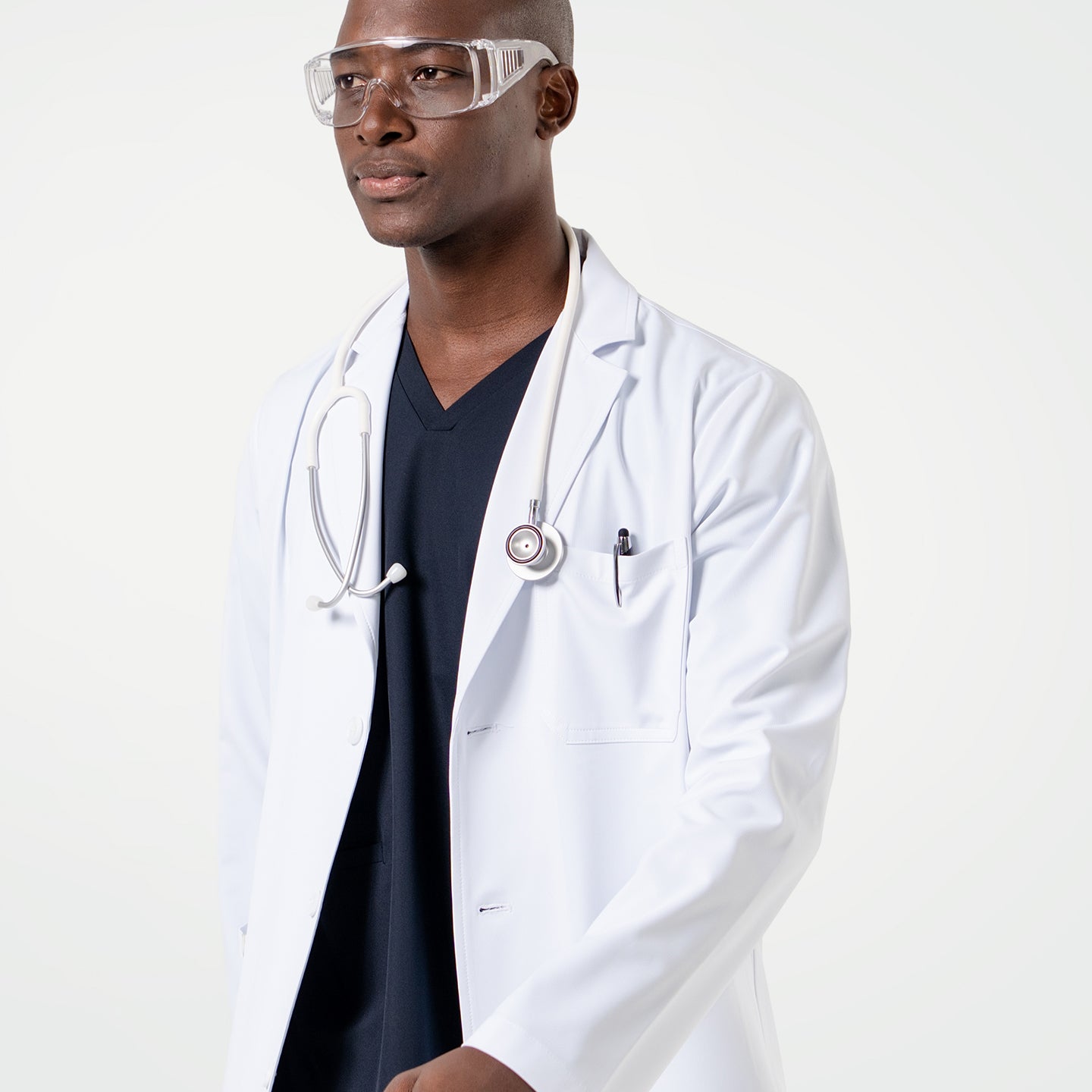 Image of Male model wearing the LCM-02 White Lab Coat over Eco Navy scrubs, accessorized with clear protective glasses and a stethoscope draped around the neck.