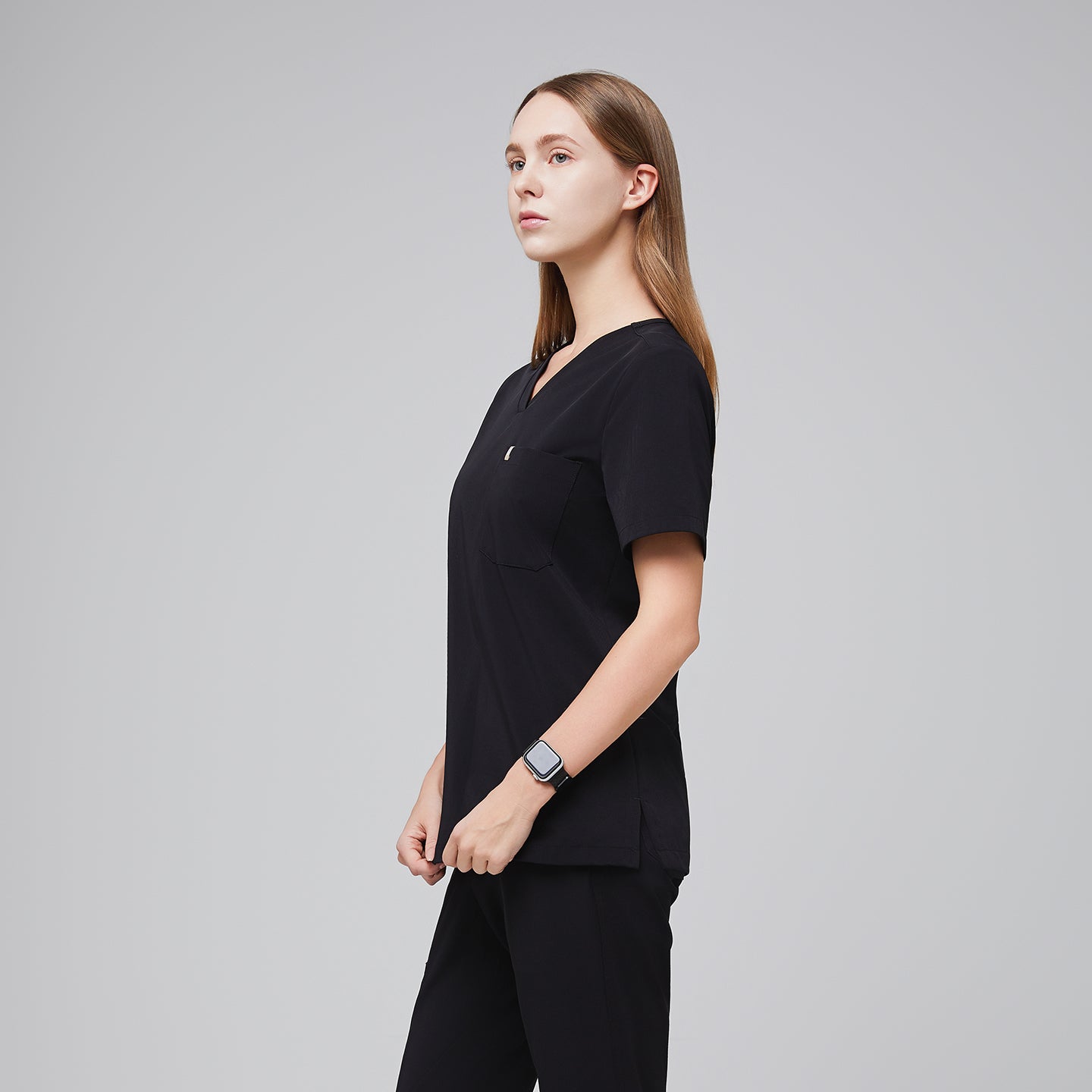 Side view of a female healthcare professional wearing a midnight black scrub set with a smart watch, standing confidently,Midnight Black