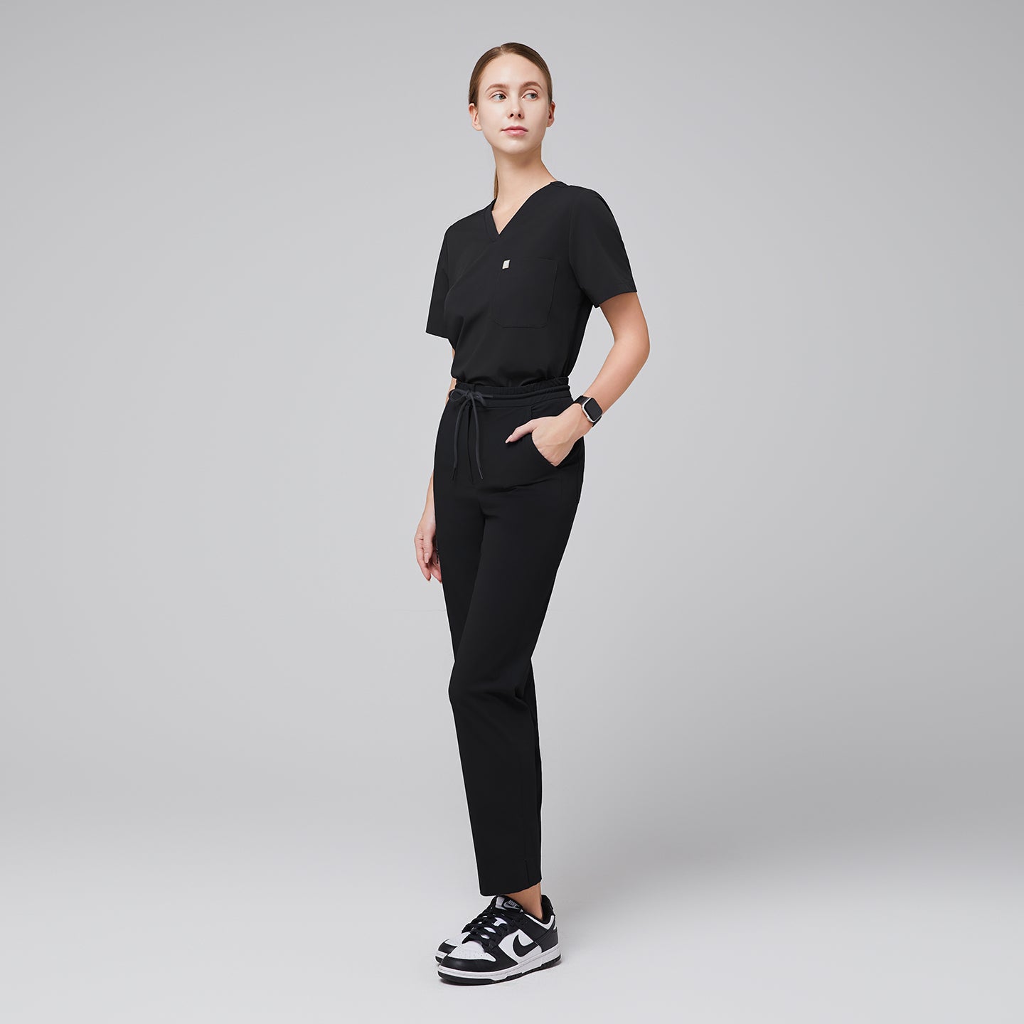 Image of Model dressed in a scrub set featuring a V-neck top and drawstring pants with zipper pockets, offering a sleek and practical design for professionals,Midnight Black