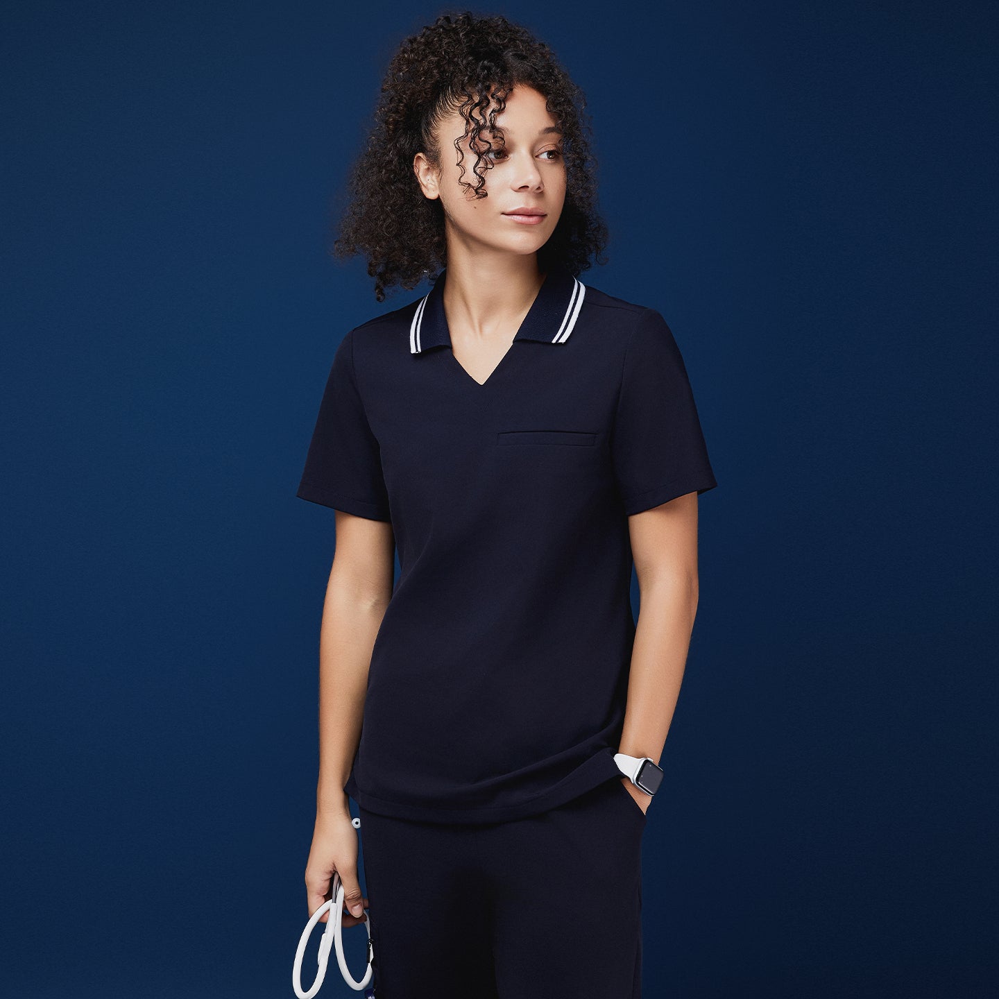 Image of Woman wearing a navy blue polo scrub top with a white striped collar, holding a stethoscope, paired with matching navy pants,Midnight Navy