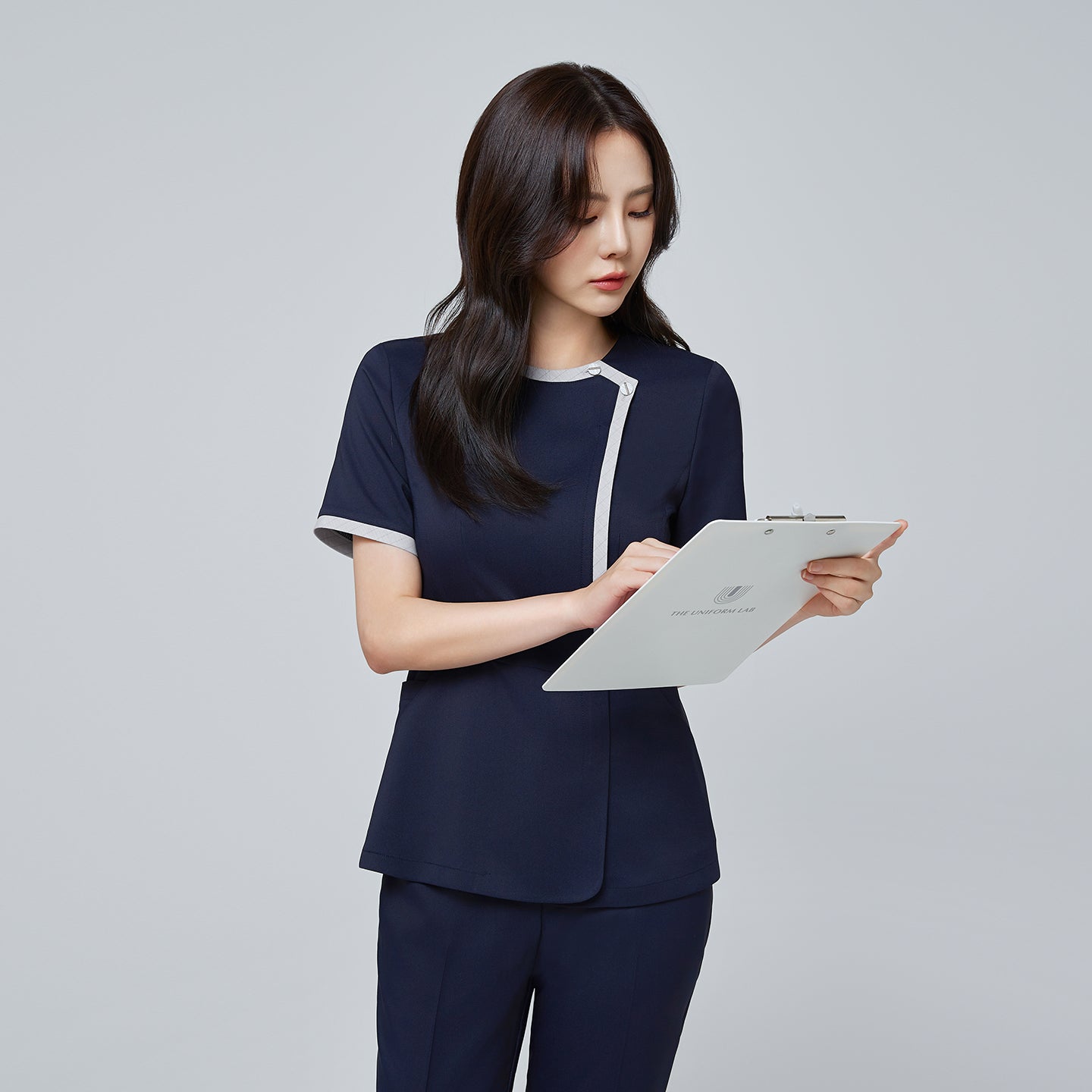 Side angle of TUL NS-174 Women’s Check Gray Round Collar Scrub Top in Mir Navy, emphasizing the contrasting gray piping on the sleeves and neckline.