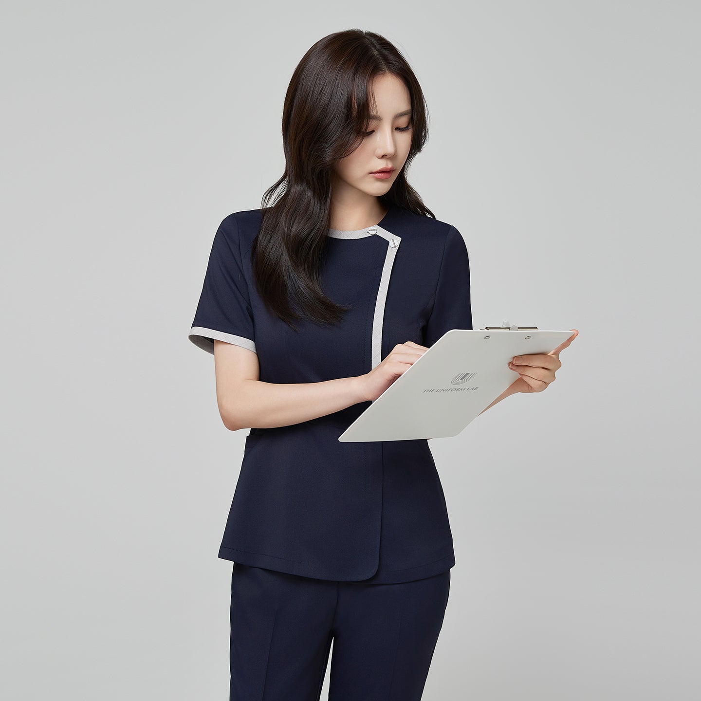Image of Side angle of TUL NS-174 Women’s Check Gray Round Collar Scrub Top in Mir Navy, emphasizing the contrasting gray piping on the sleeves and neckline.