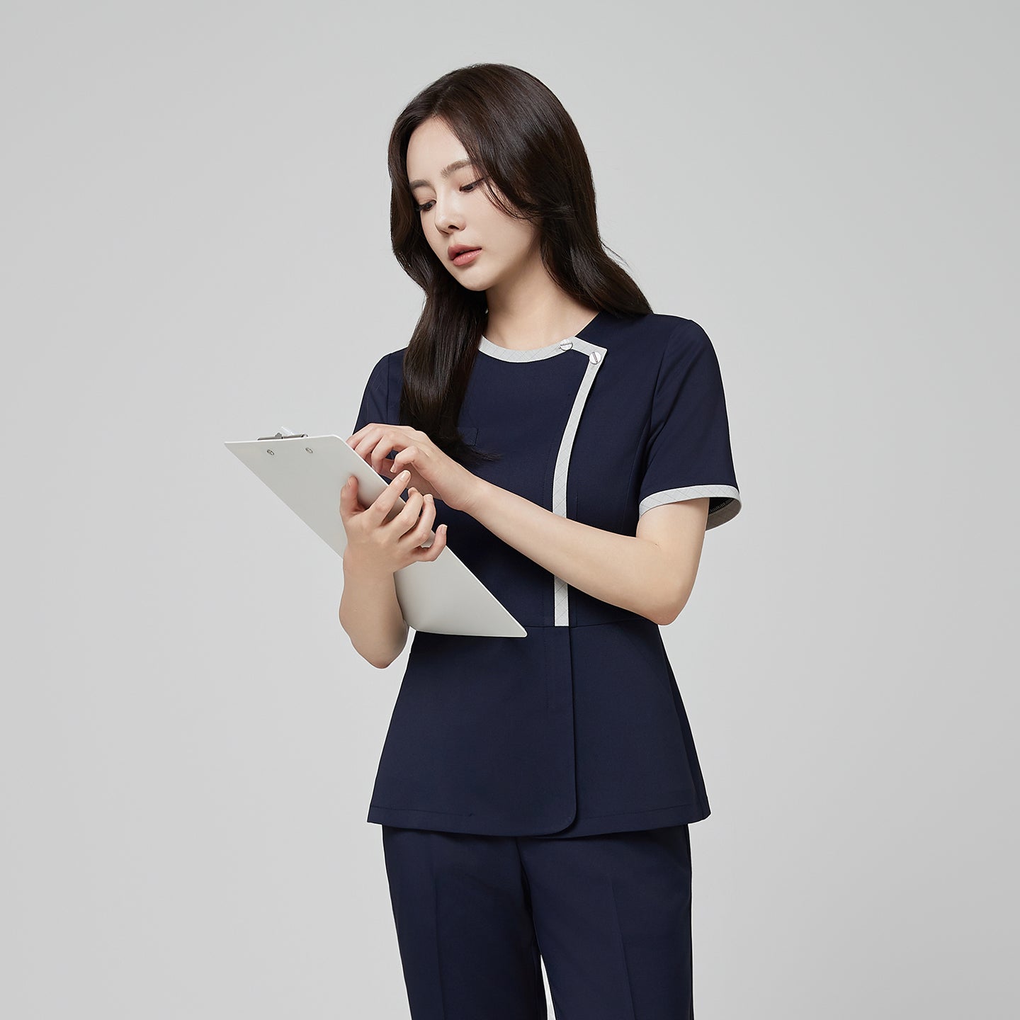 Model wearing TUL NS-174 Women’s Check Gray Round Collar Scrub Top in Mir Navy, featuring a contrasting gray trim around the neckline and front.