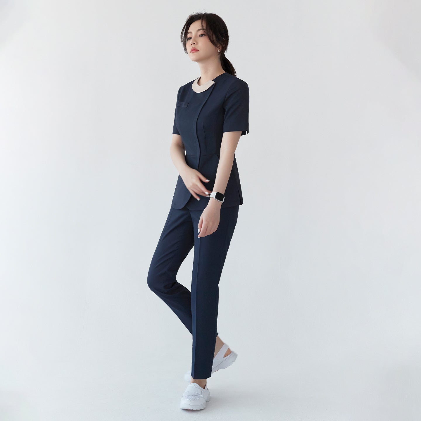 Image of A woman in a navy round-neck front zipper top and matching pants, standing with a hand on her stomach. She wears white shoes and a smartwatch,Mir Navy
