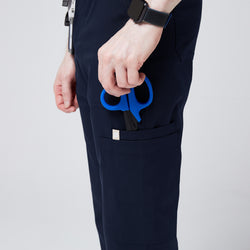 Image of Close-up of navy jogger scrub pants with a side pocket holding blue medical scissors, showcasing functionality and utility.Navy