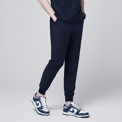 Image of Side view of navy jogger scrub pants with 8 pockets, cuffed ankles, and hands in pockets, paired with navy sneakers,Navy