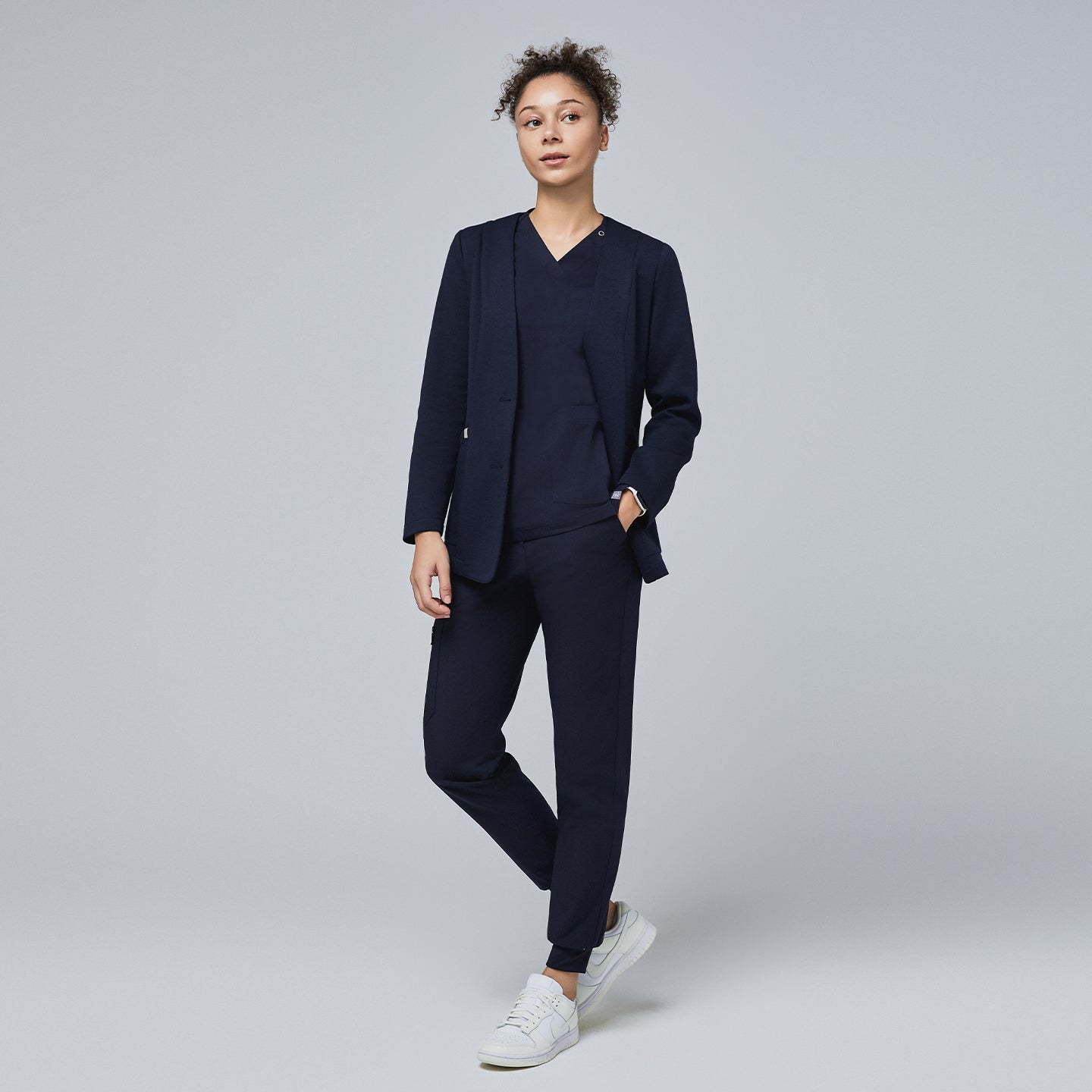 Image of Woman wearing a navy comfort cardigan over a matching V-neck scrub top and jogger scrub pants, paired with white sneakers for a professional yet relaxed look,Navy
