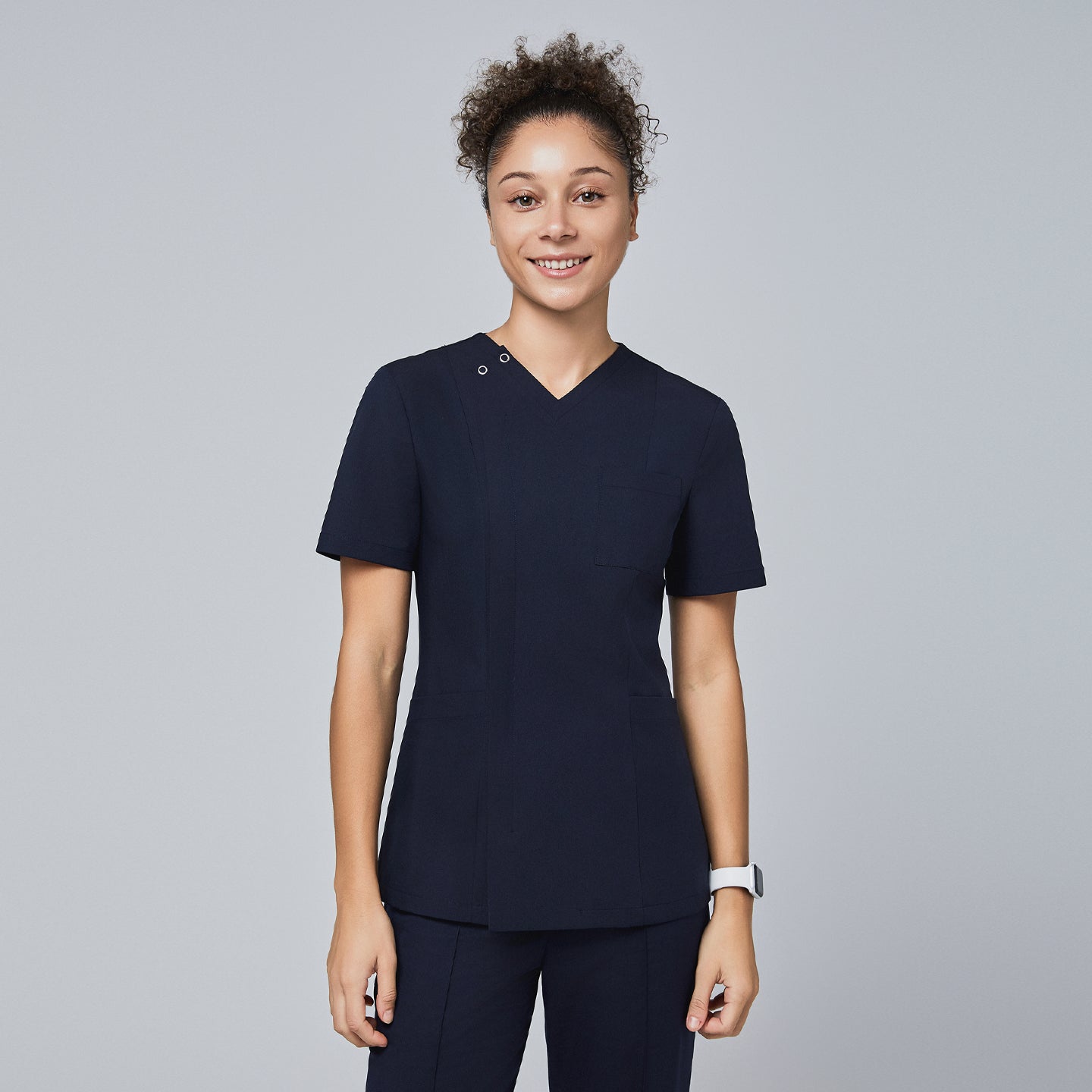 Image of Female model wearing a navy V-neck scrub top with a subtle front zipper, short sleeves, chest pocket, and a fitted design, standing and smiling,Eco Navy