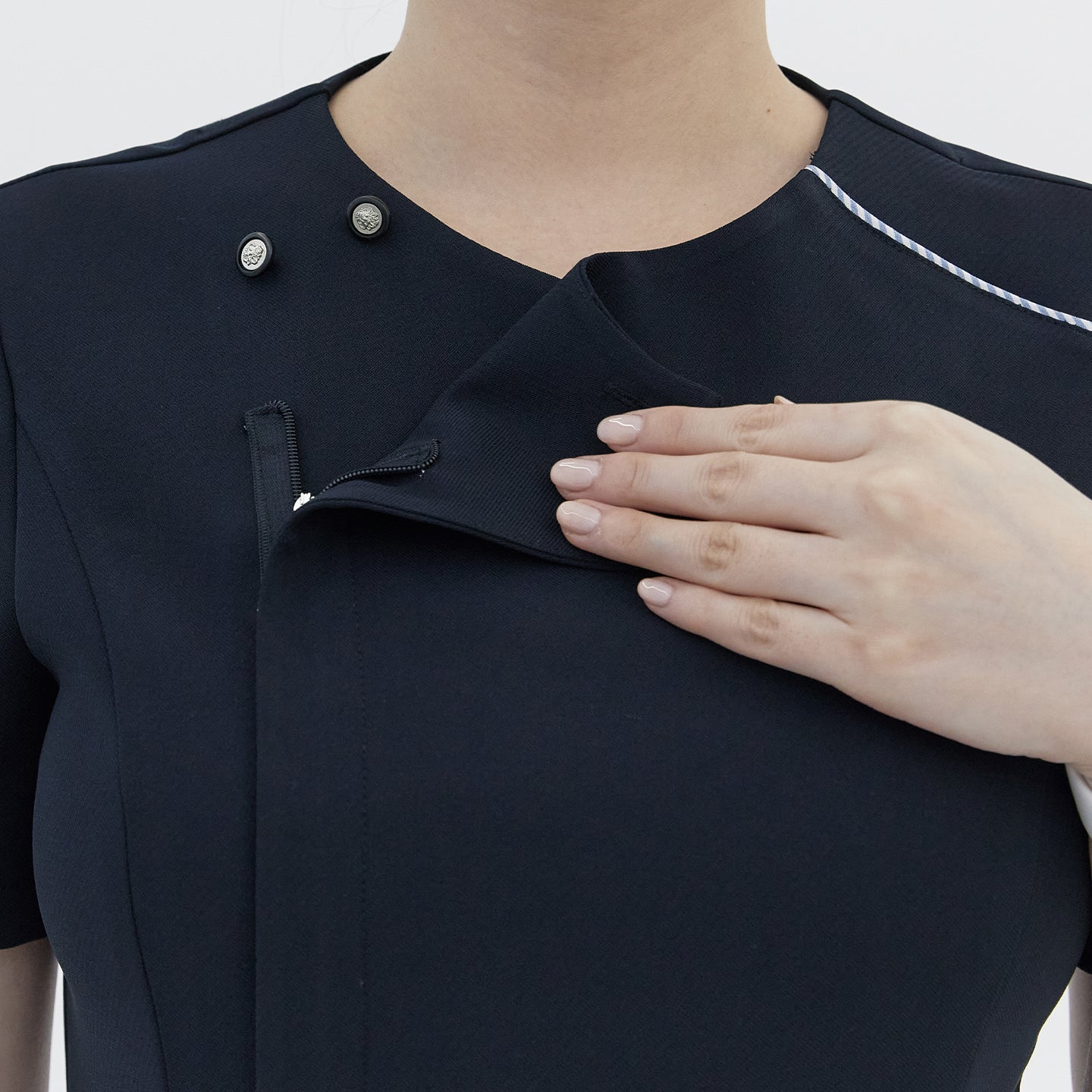 Image of A close-up of a woman’s hand opening the front zipper of a navy round-neck top, revealing a hidden button detail and white trim,Navy
