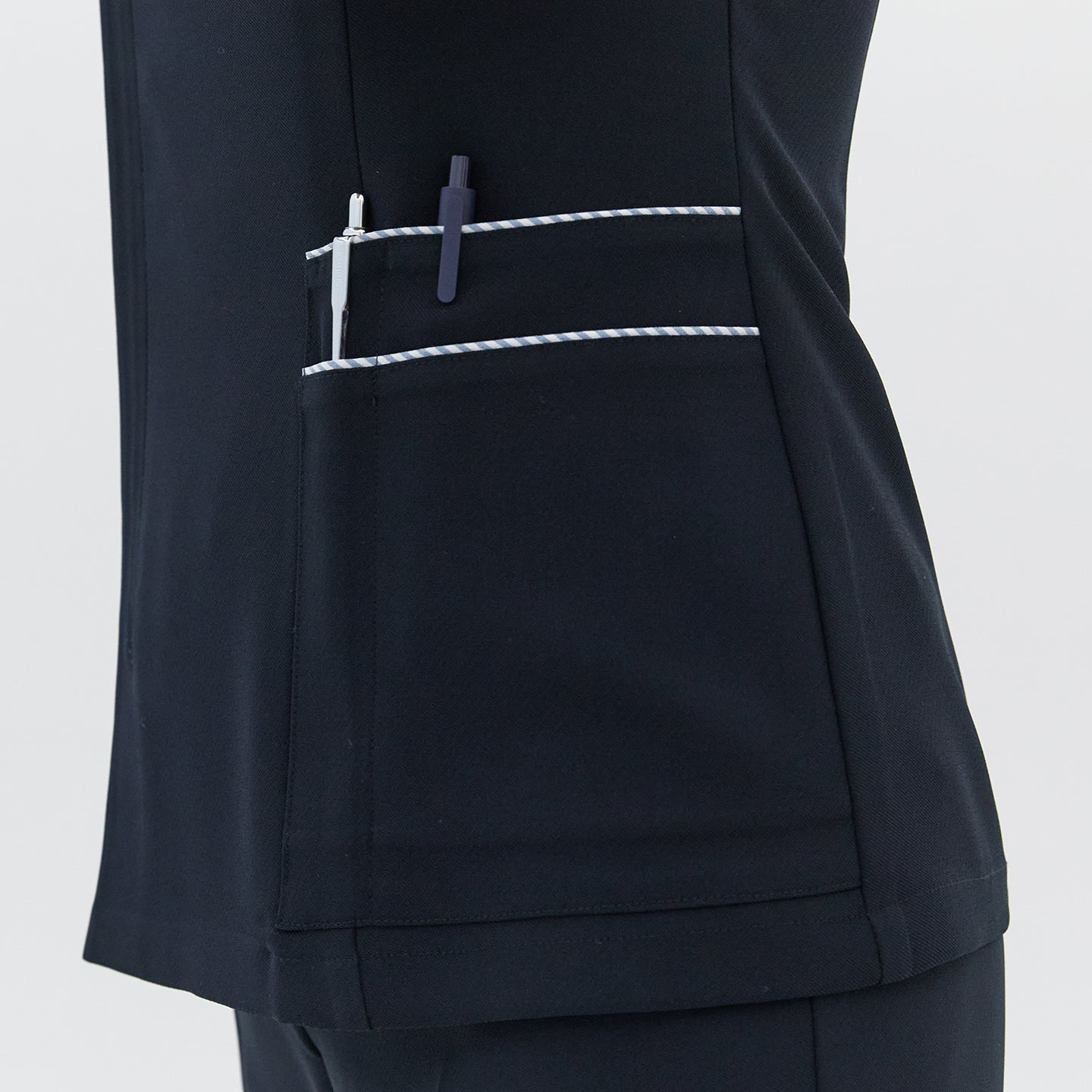 Image of  A detailed view of the side pocket on a navy round-neck top, featuring white trim and holding two pens,Navy