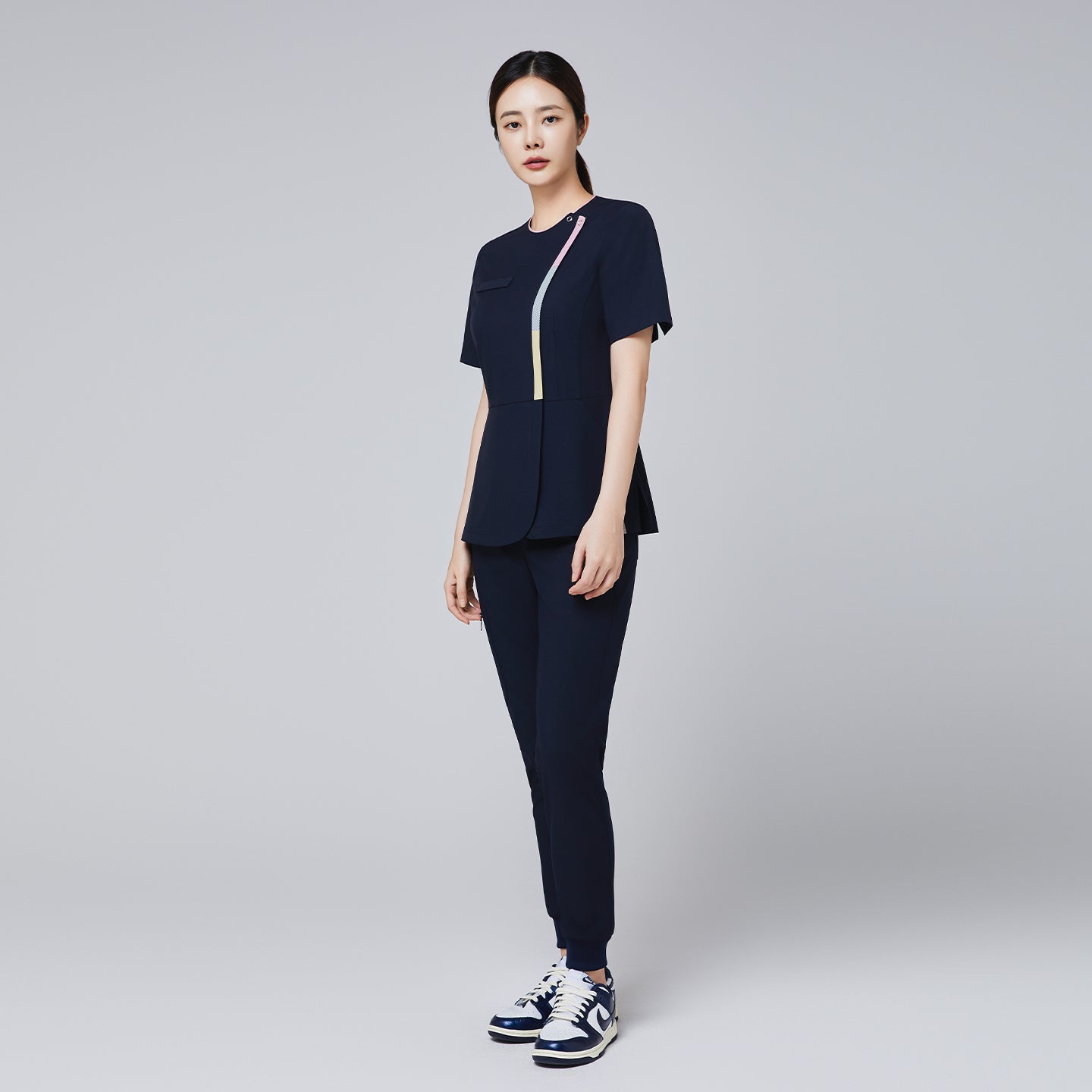 Full-body view of a woman wearing a navy scrub set with gradient zipper detail, paired with athletic sneakers,Navy