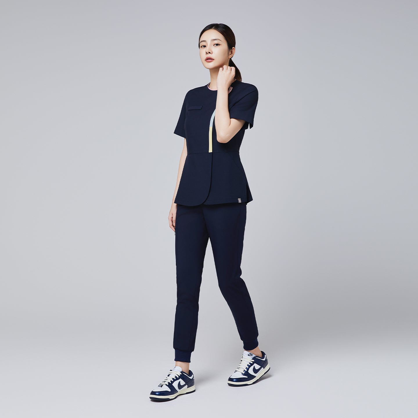 Image of Full-body view of a woman wearing a navy scrub set with gradient front zipper detail and sporty sneakers,Navy