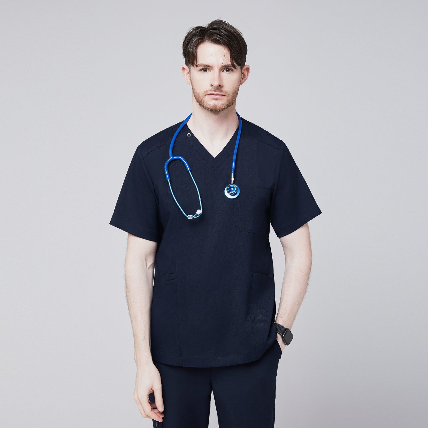 Front view of a man wearing a navy scrub top with a front zipper, featuring a blue stethoscope draped around his neck,Navy