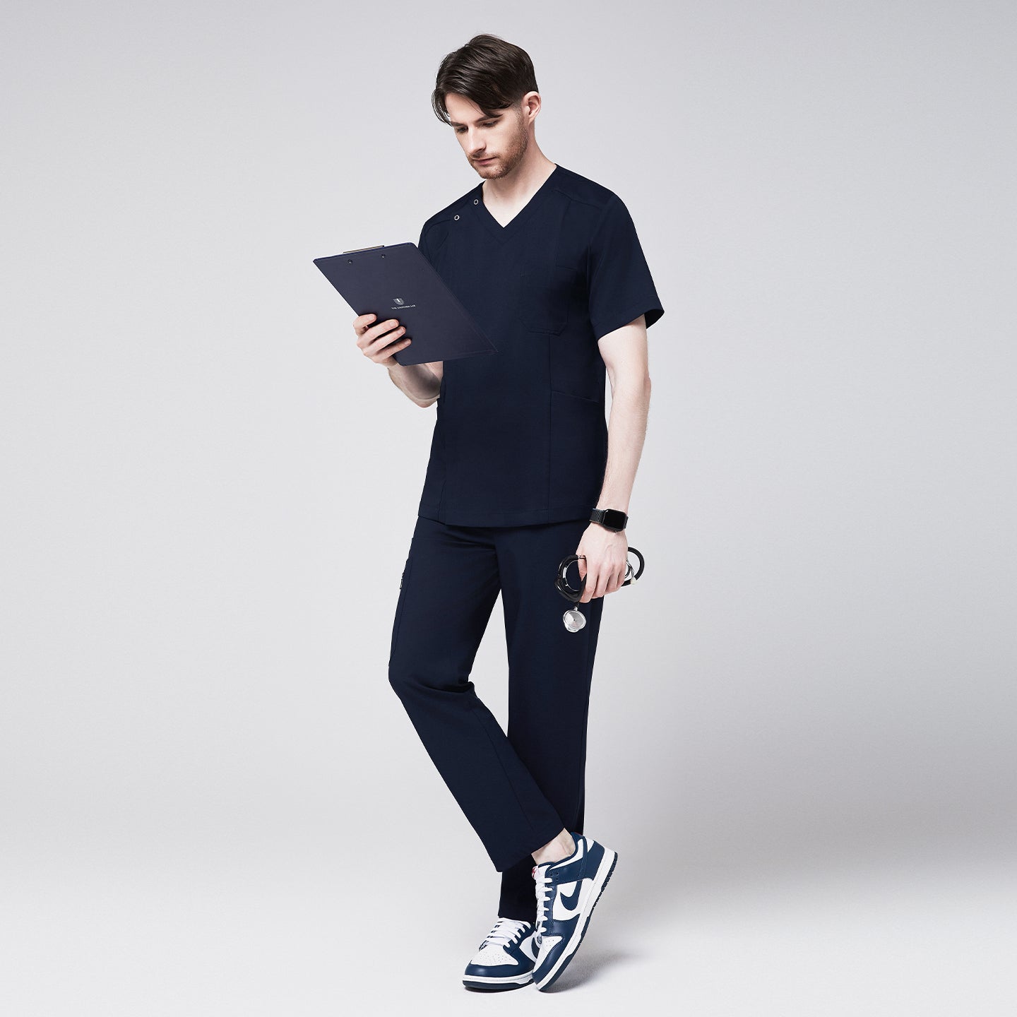 Image of Man wearing a navy scrub set, holding a clipboard and stethoscope, showcasing the professional and modern design of the uniform, while standing in a relaxed pose,Navy