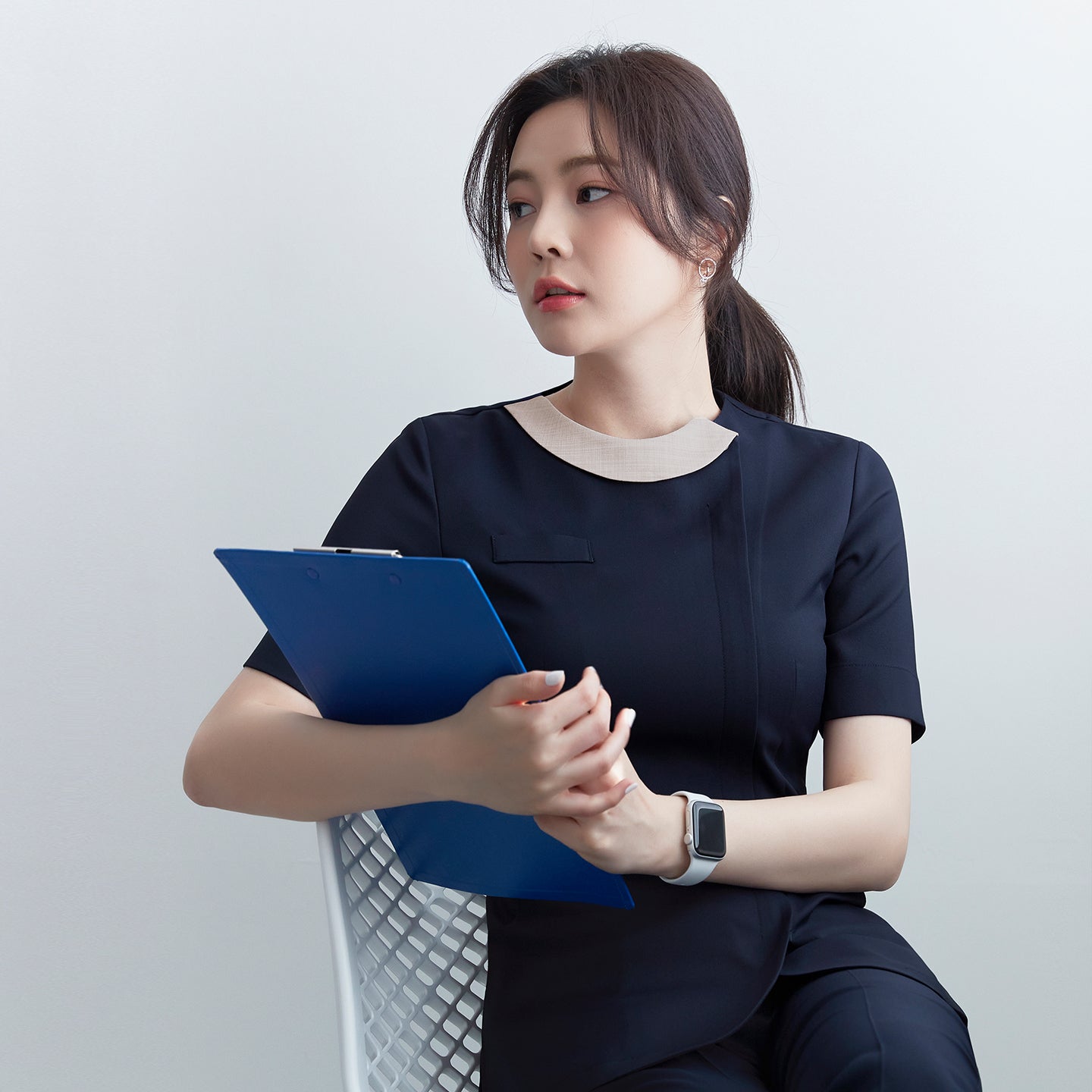 Image of Model seated wearing TUL NS-150 Navy scrub top with a contrasting round collar, holding a clipboard for a professional look.