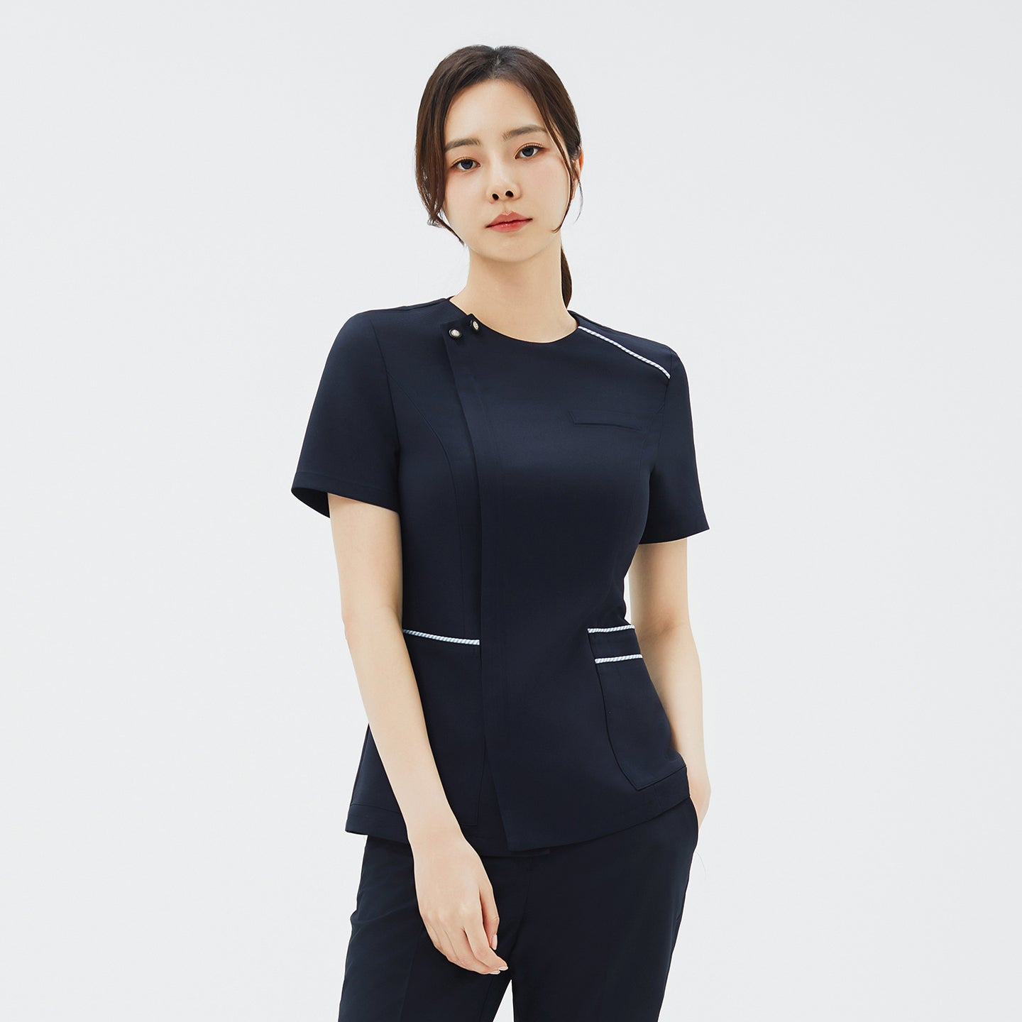 Image of Front view of a woman wearing a navy short-sleeve scrub top with snap buttons at the collar and subtle white piping on the pockets,Navy