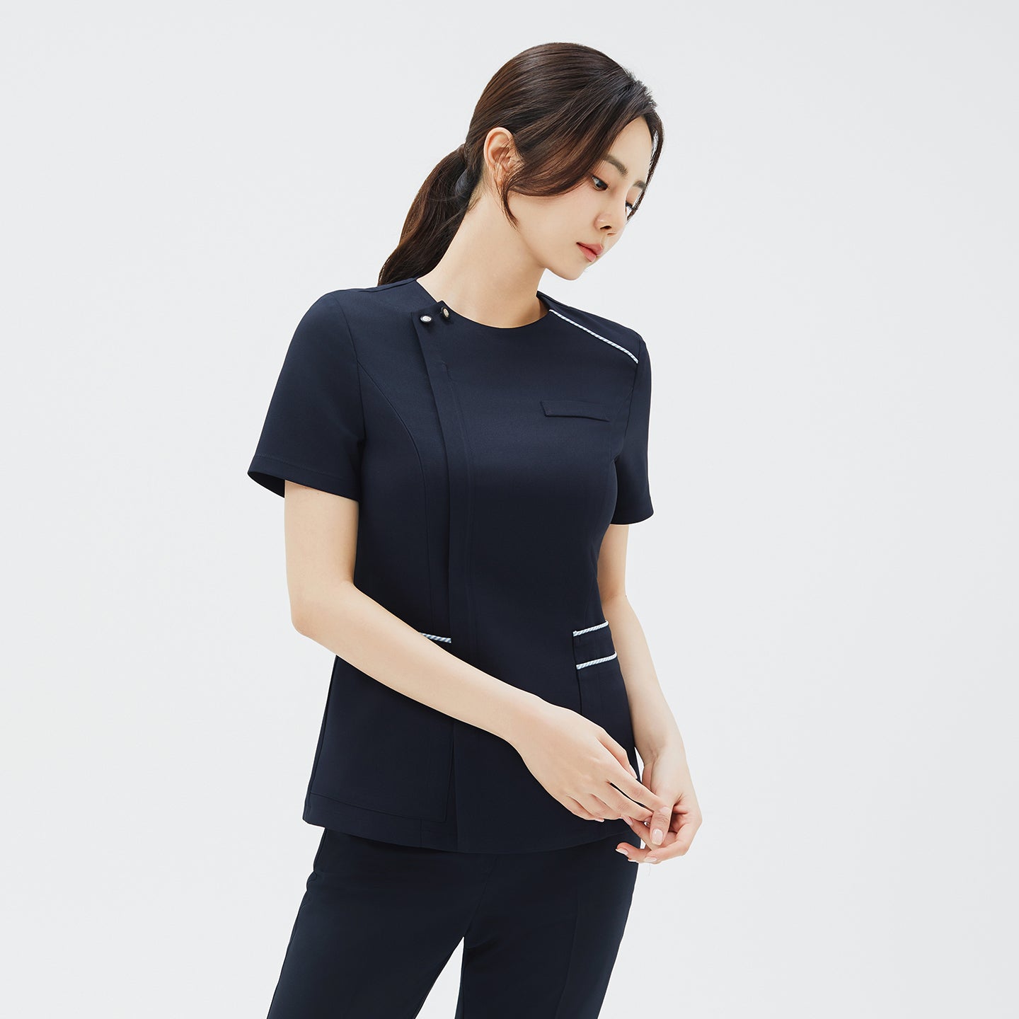 Image of Closer side angle of a woman wearing a navy scrub top with short sleeves and a discreet front zipper, highlighting the fitted silhouette,Navy