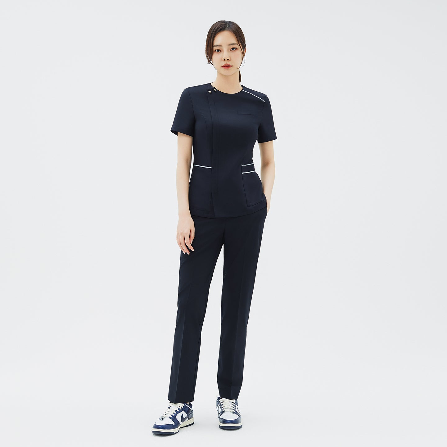 Image of Full-body shot of a woman dressed in a matching navy scrub top and pants, paired with casual sneakers,Navy