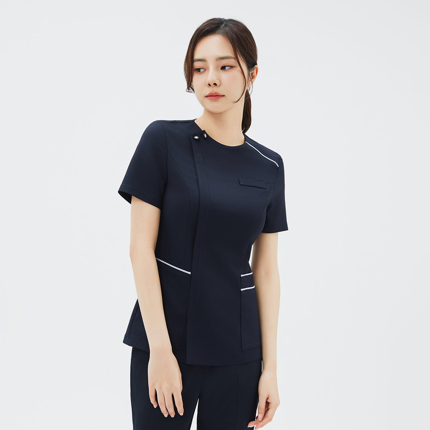 Image of Slight angled front view of a woman in a navy scrub top showing the hidden front zipper closure and chest pocket detail,Navy