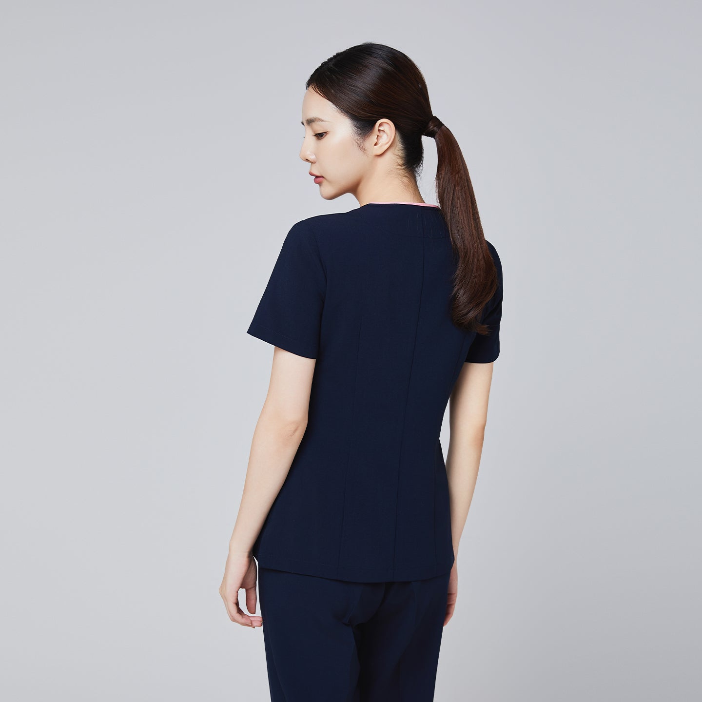 Image of Back view of a navy scrub top with short sleeves and a streamlined, tailored fit, modeled by a woman,Navy