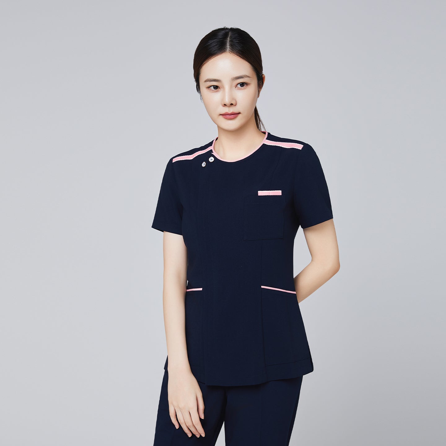 Image of Navy scrub top with pink edge detailing and front pocket, modeled by a woman for professional settings,Navy